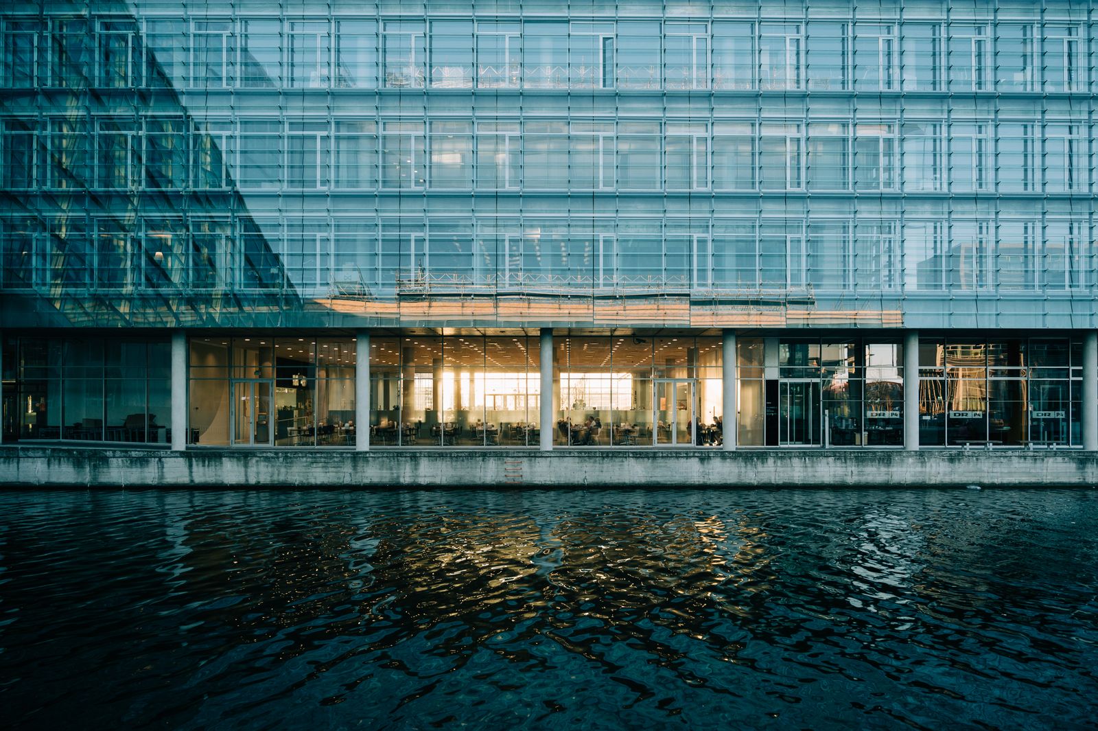 Moderne bygning med glasfacade, der spejler sig i vandet, dansk arkitektur